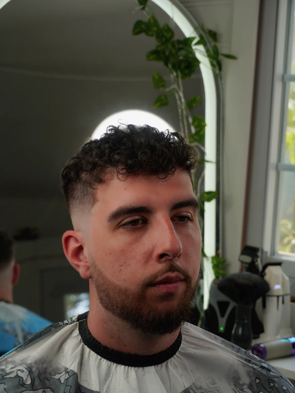 The same client after — curls kept on top, mid fade through the sides, beard lined up