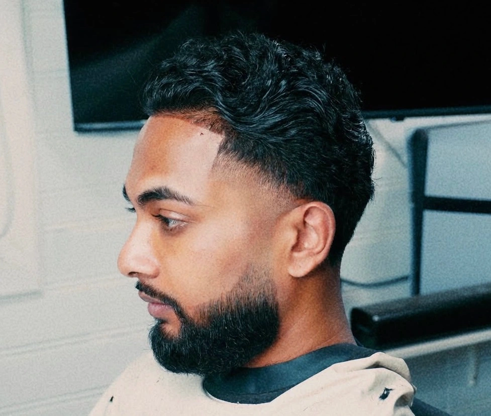Low taper fade with a wavy top, beard tapered and lined into the cheek